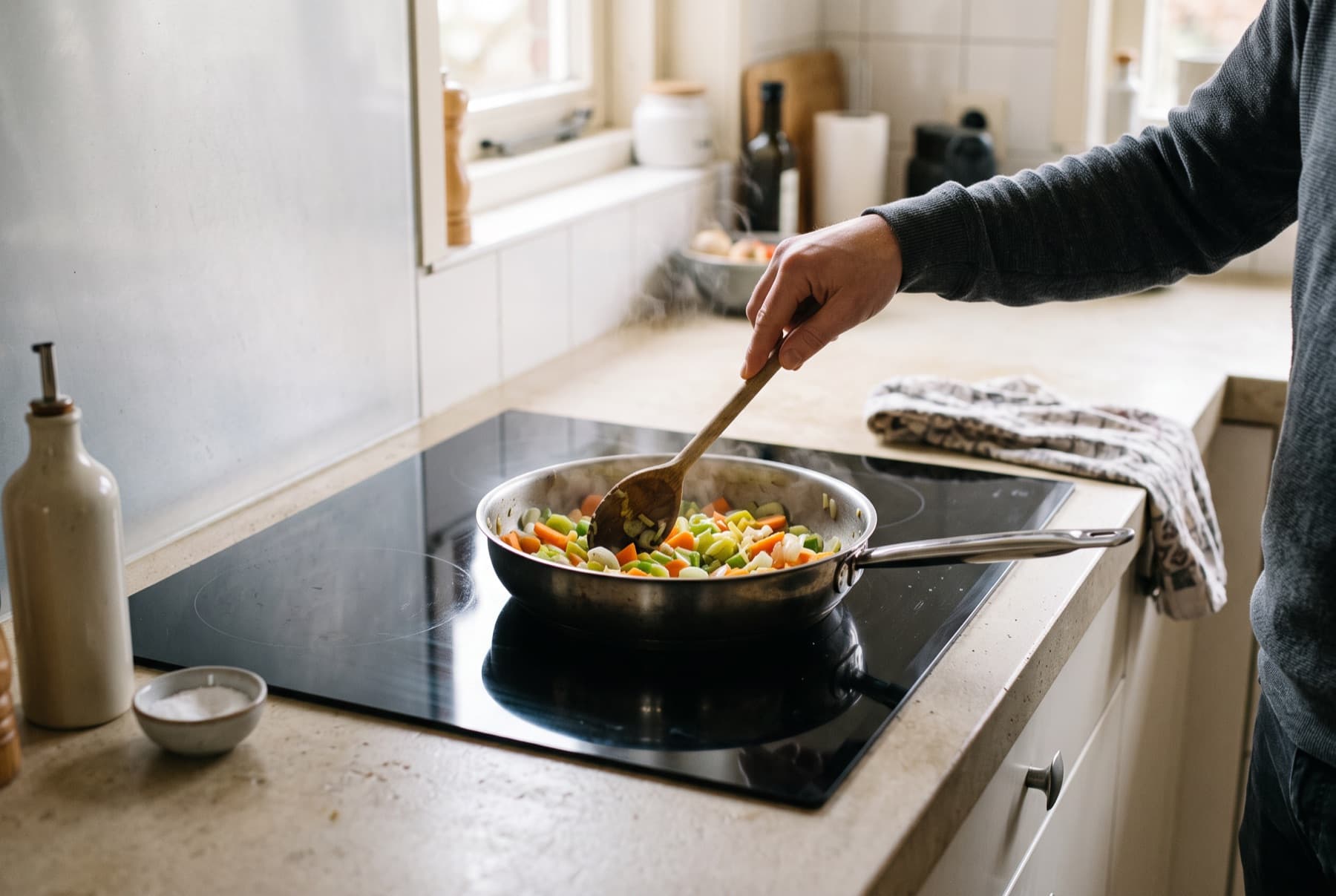 Iemand roerbakt groenten in een pan op een inductiekookplaat