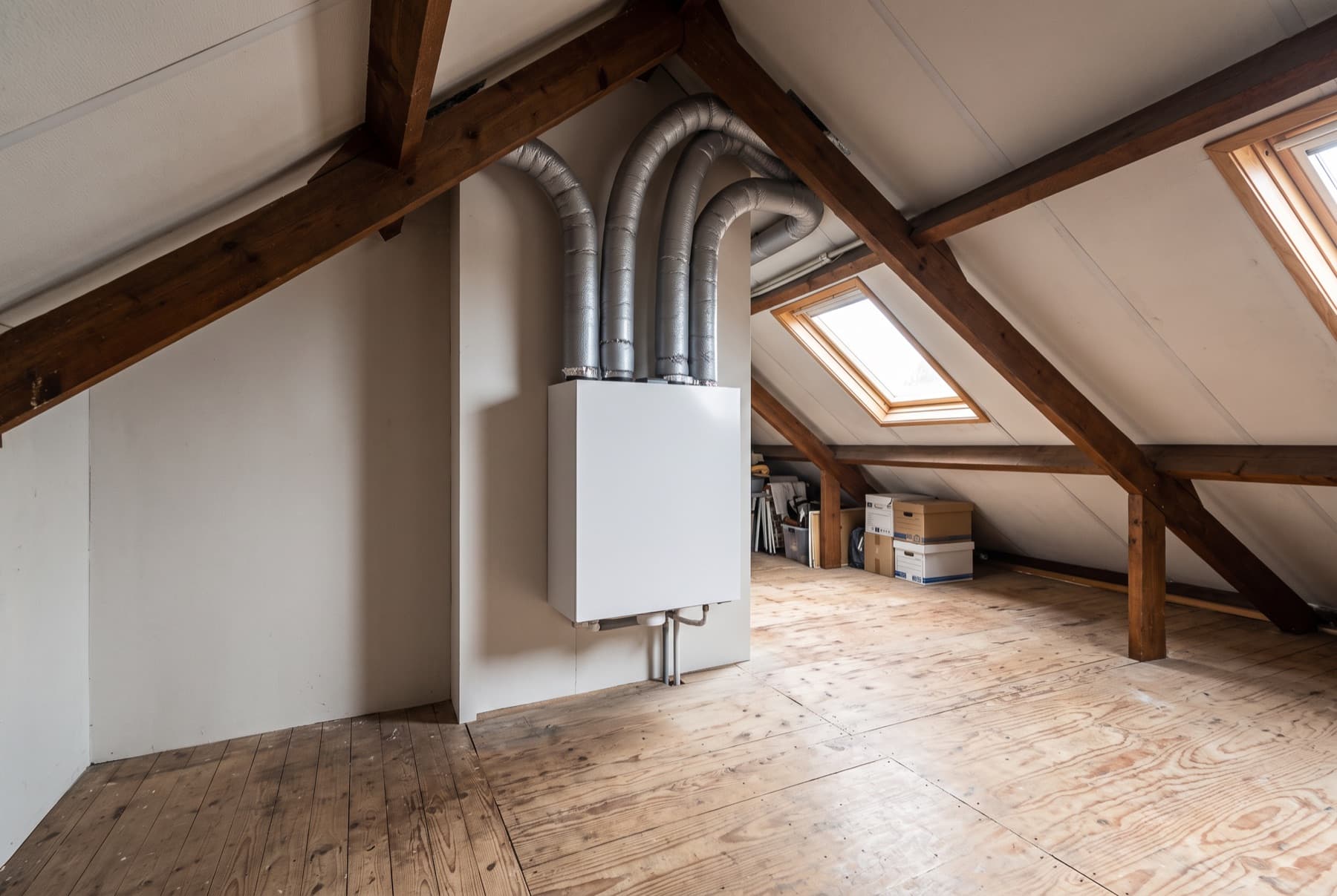 Wtw-unit met vier ventilatiekanalen aan de wand van een zolder