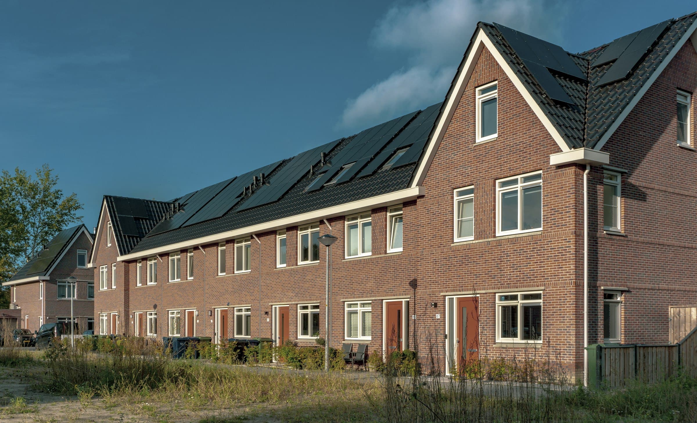 Rij nieuwe bakstenen rijtjeshuizen met witte kozijnen en zonnepanelen op het dak